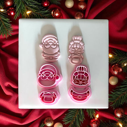 Santa and Mrs Claus clay cutters with pink clay impressions side by side on white tile