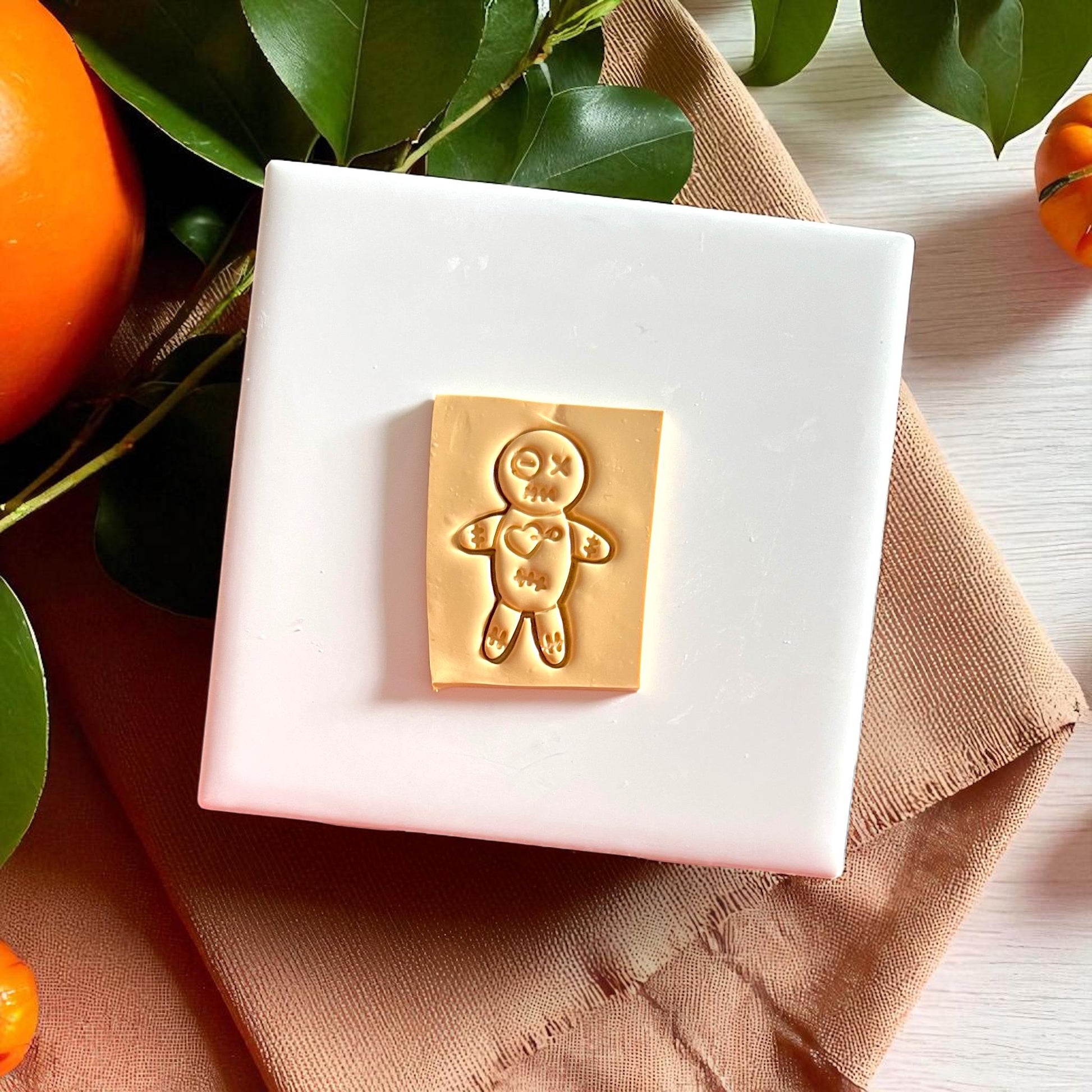 Yellow voodoo doll clay imprint on white slab with leaves