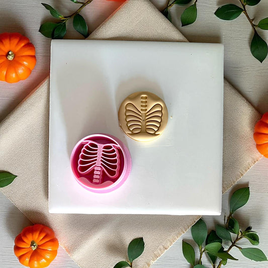 Pink ribcage skeleton clay cutter next to golden clay piece