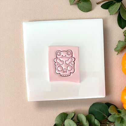 Pink frog on skull clay impression on white tile