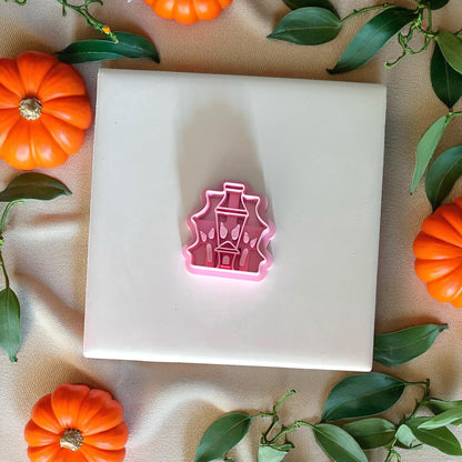 Pink haunted house clay cutter on white tile with pumpkins