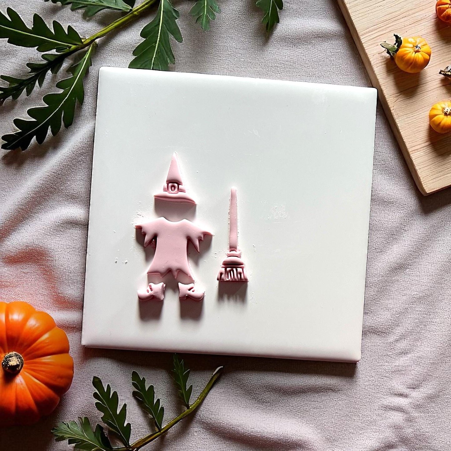 Witch clay imprint with hat broom and shoes on white tile with pumpkins