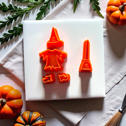 Orange witch clay cutters with broom hat dress and shoes on white tile