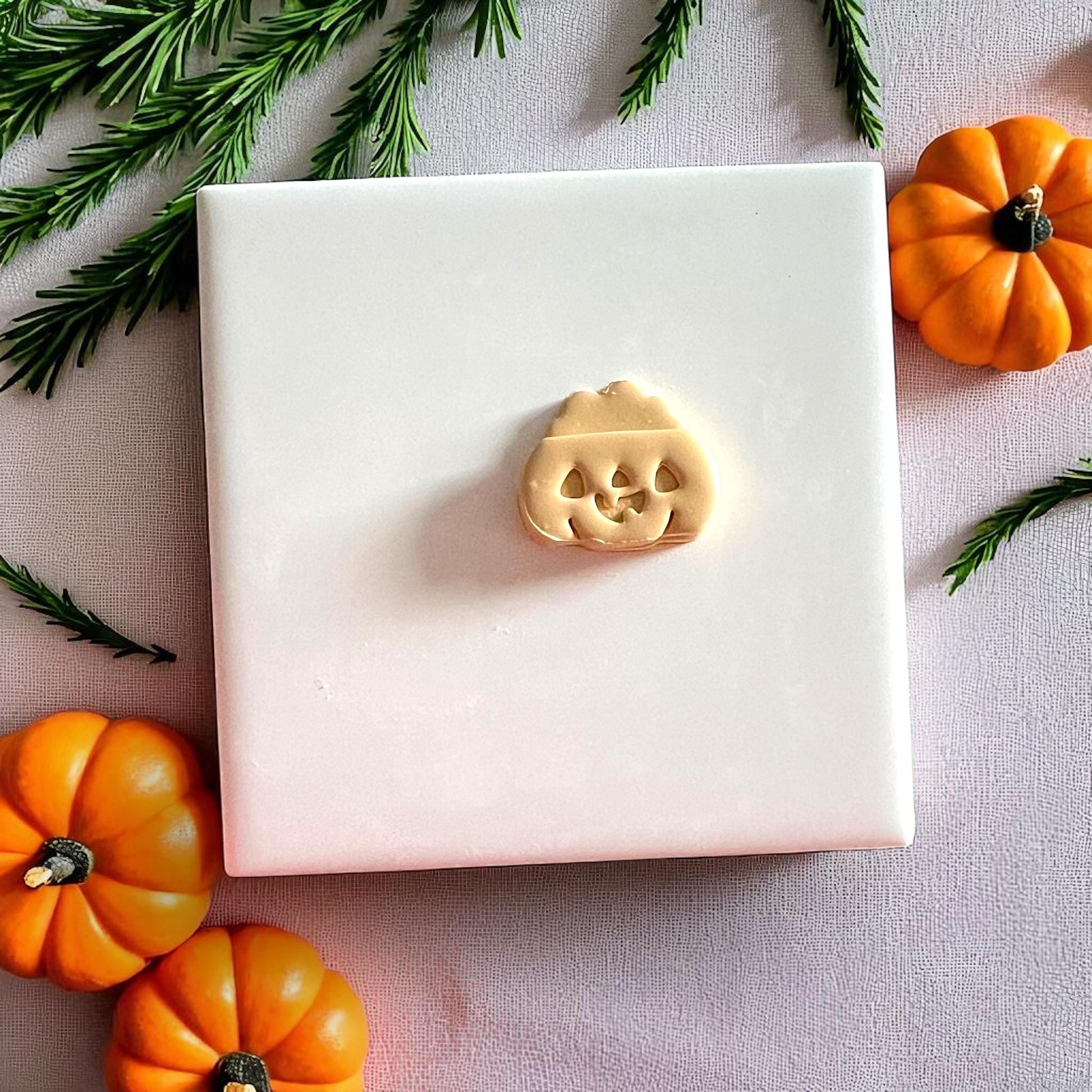 Small jack o lantern pumpkin clay cutout on white tile with mini pumpkins