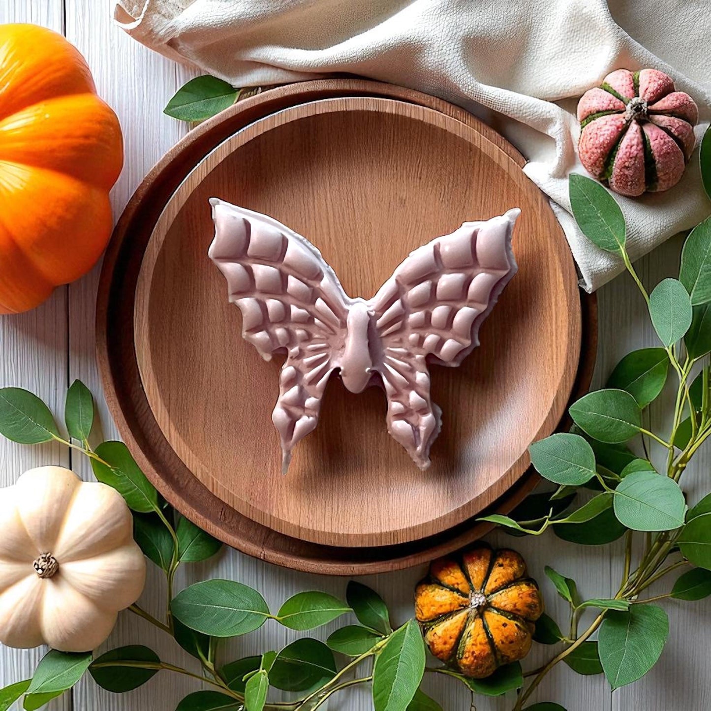 Large clay butterfly with spiderweb wings on wooden plate surrounded by pumpkins