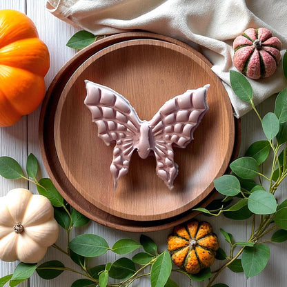 Large clay butterfly with spiderweb wings on wooden plate surrounded by pumpkins