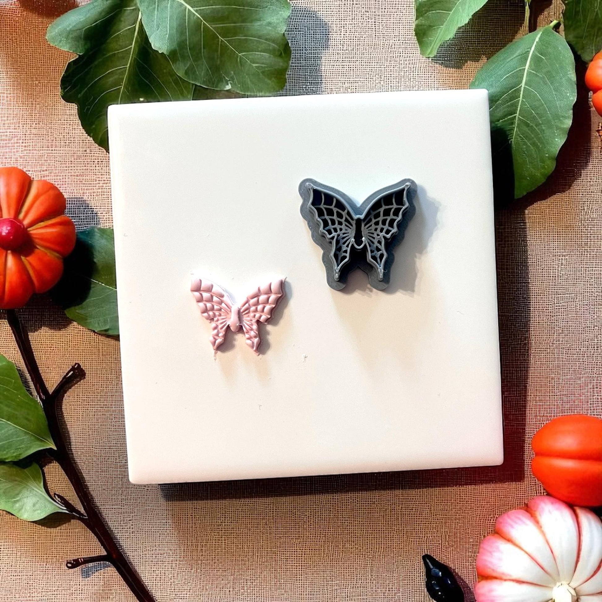 Spiderweb butterfly clay cutter and clay impression on white tile with leaves and pumpkins