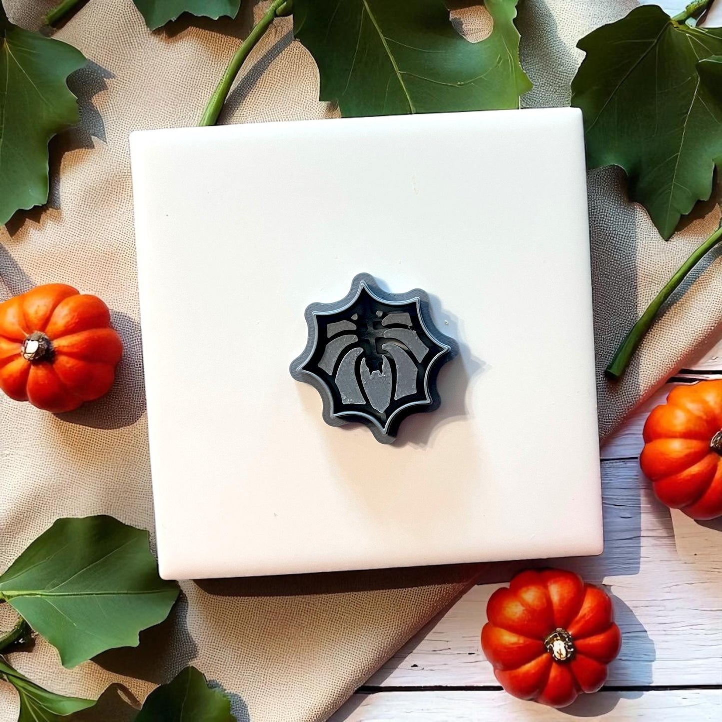 Spider web clay cutter on white tile with pumpkins and leaves