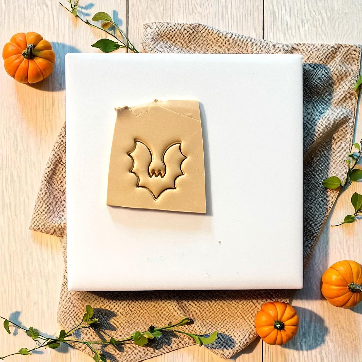 Bat clay imprint pressed into beige clay sheet with pumpkins and greenery