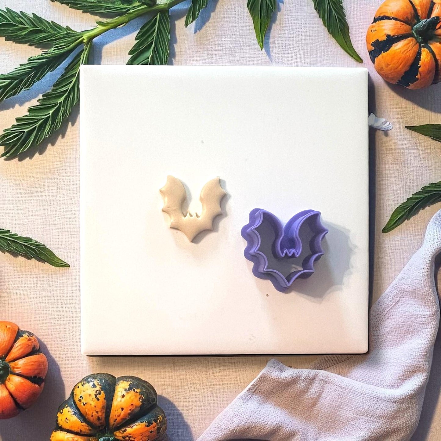 Bat clay imprint next to purple bat clay cutter on white tile with pumpkins