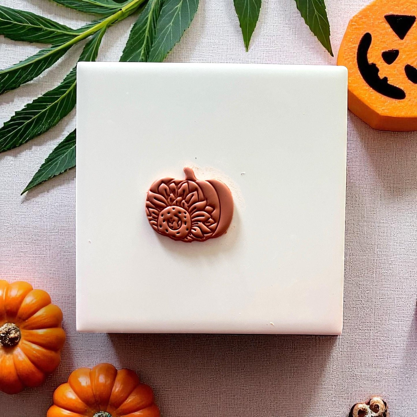 Clay sunflower pumpkin piece on white tile with mini pumpkins