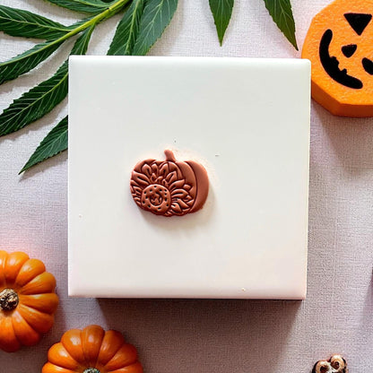 Clay sunflower pumpkin piece on white tile with mini pumpkins