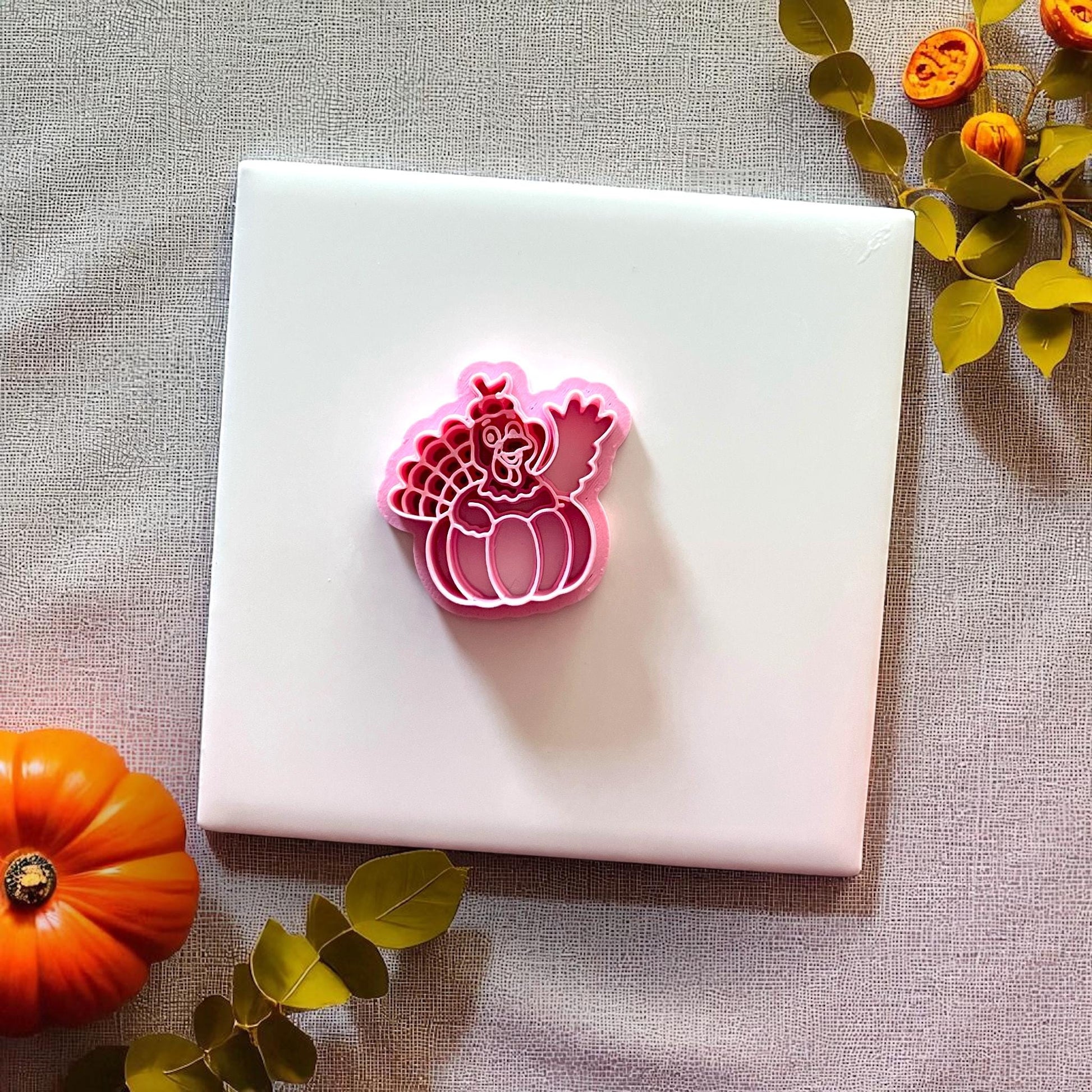 Pink turkey pumpkin clay cutter on white tile with fall decor