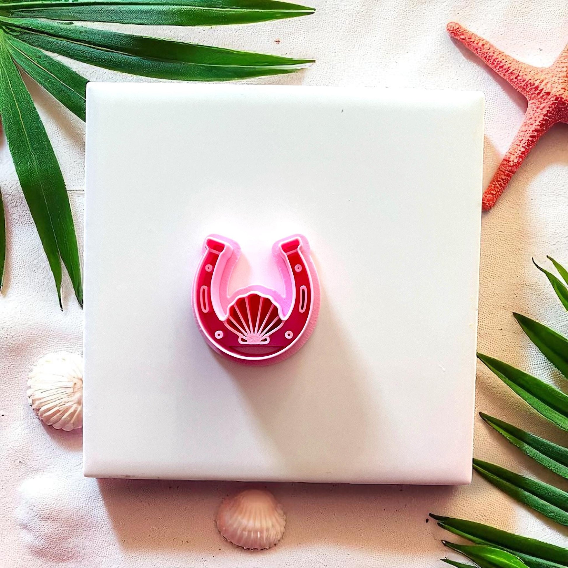 Red horseshoe seashell polymer clay cutter on white tile