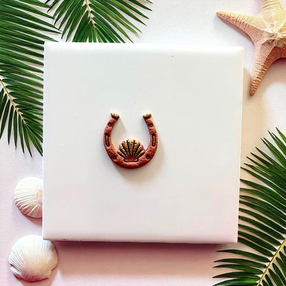 Small clay horseshoe seashell design on white tile with starfish and palm leaves