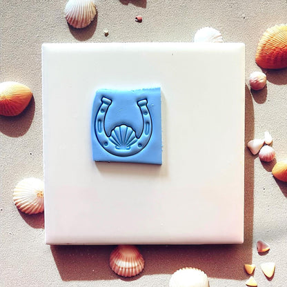 Blue clay horseshoe seashell impression on white tile with seashells around