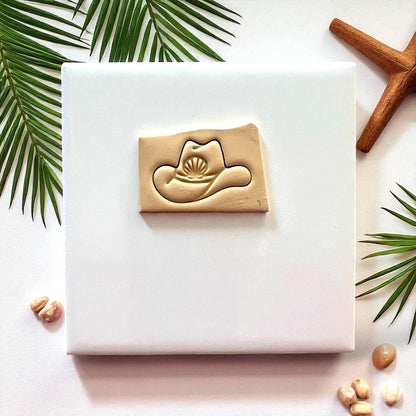 Clay cowboy hat seashell impression on beige clay slab surrounded by seashells