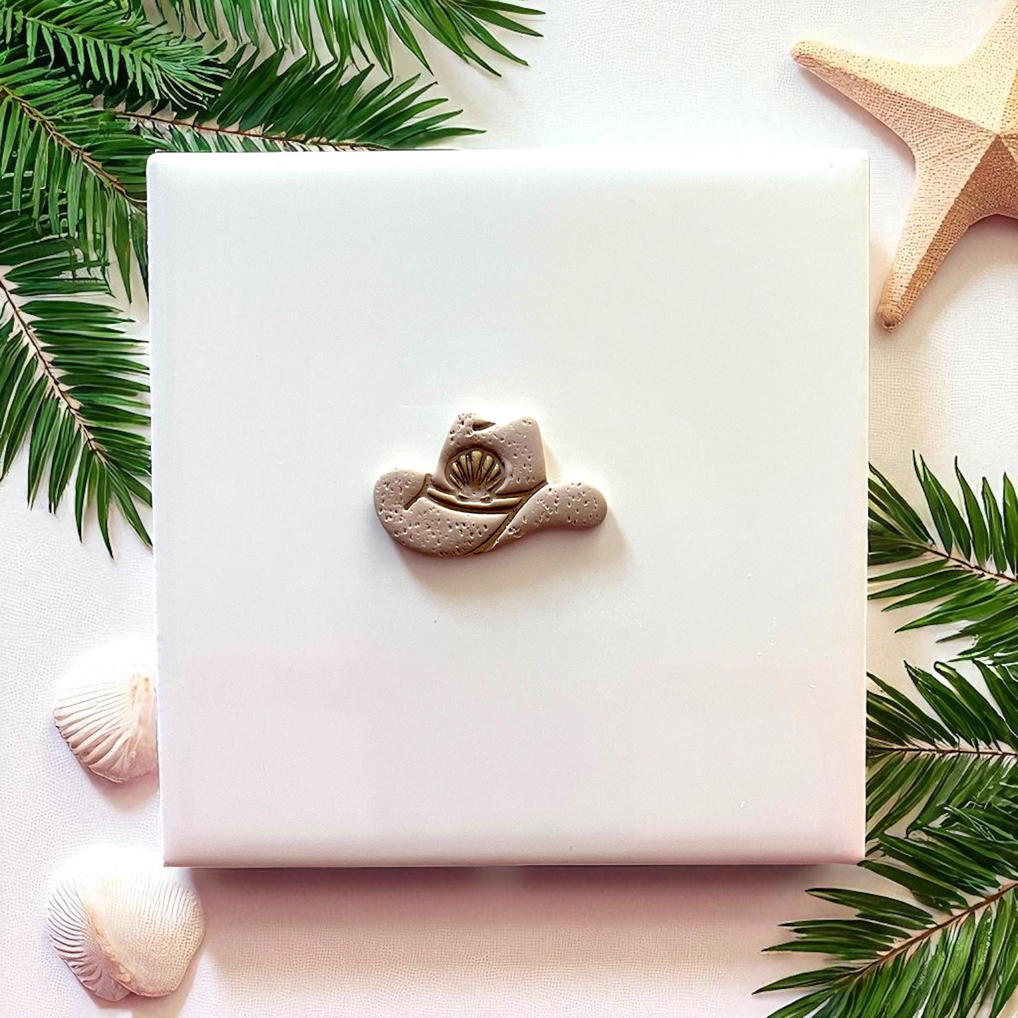 Small cowboy hat clay piece with seashell detail on white tile and starfish decor