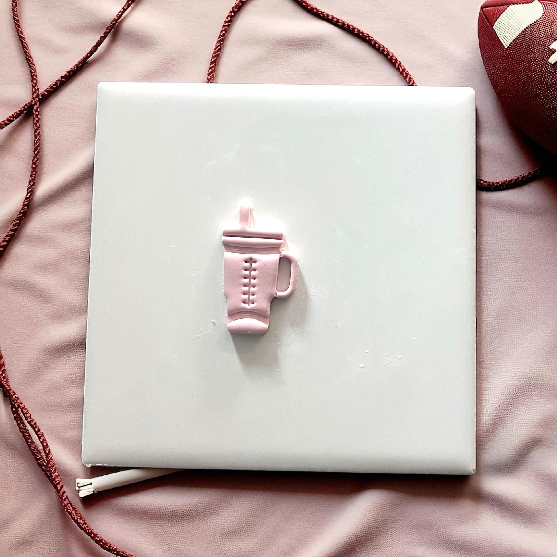 Small pink football Stanley tumbler clay piece on white tile