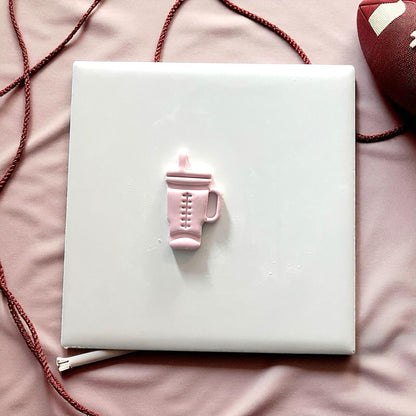 Small pink football Stanley tumbler clay piece on white tile
