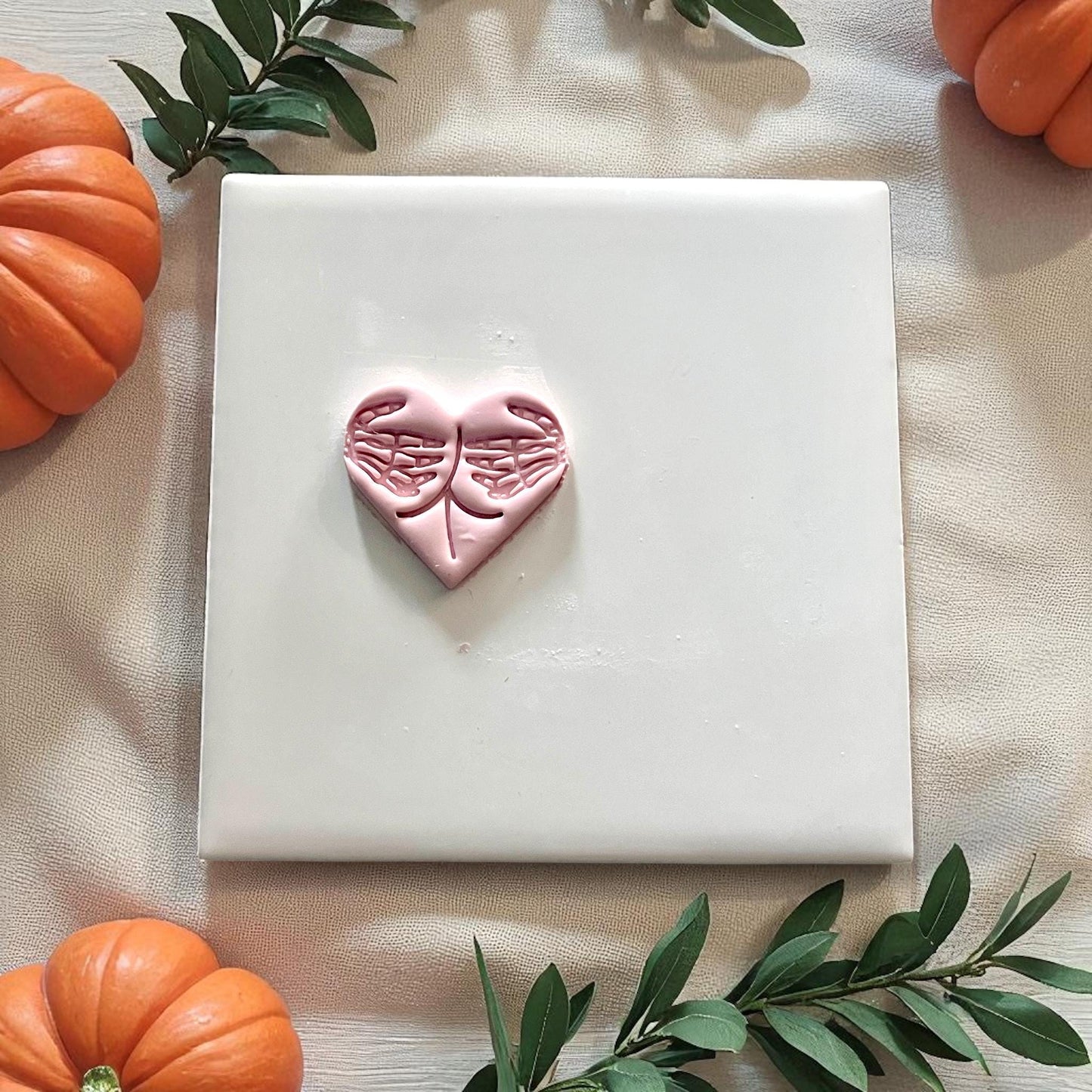 Small heart clay piece with skeleton hand design on white tile