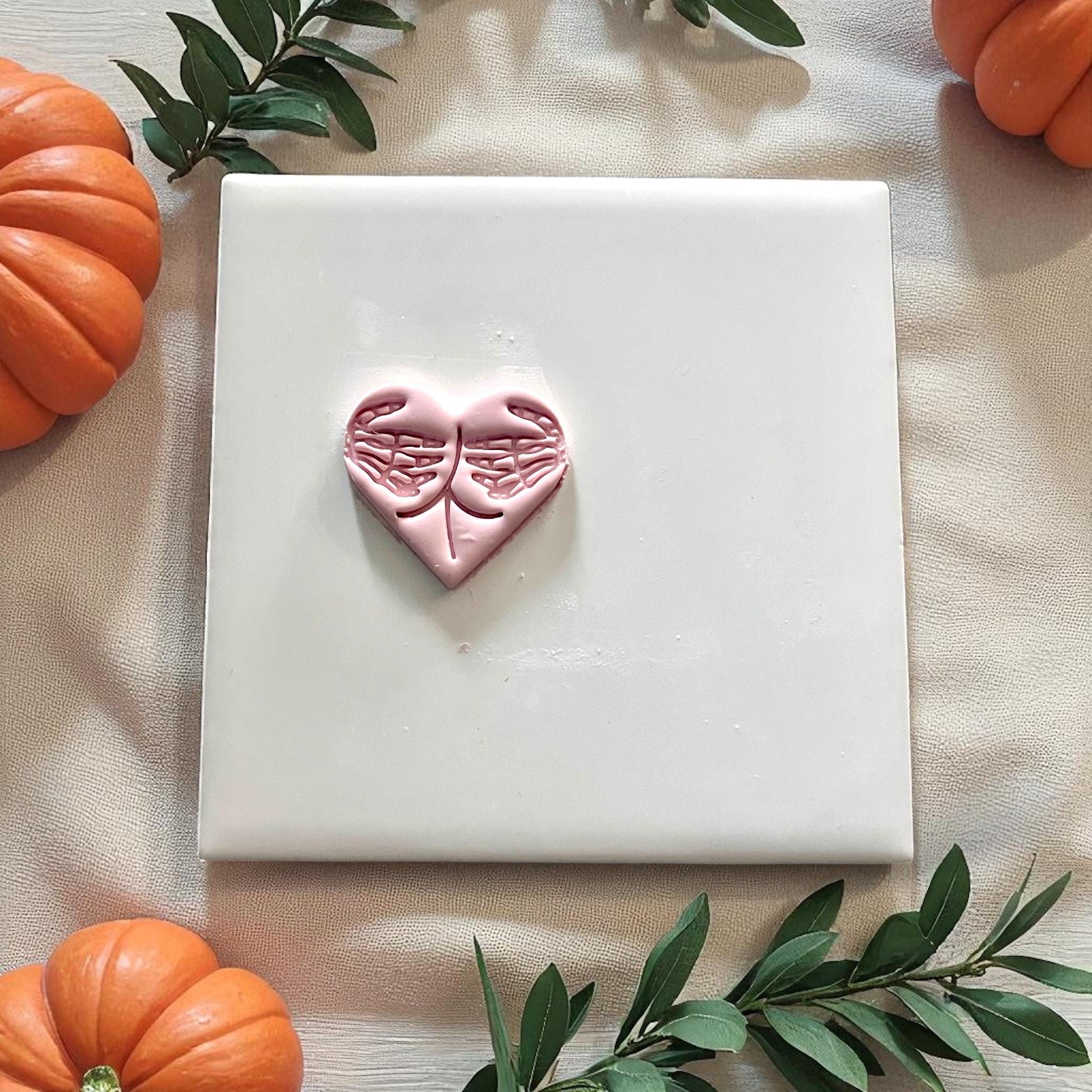 Small heart clay piece with skeleton hand design on white tile