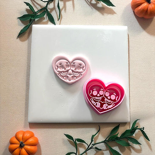 Pink skeleton couple heart clay piece with cutter beside it