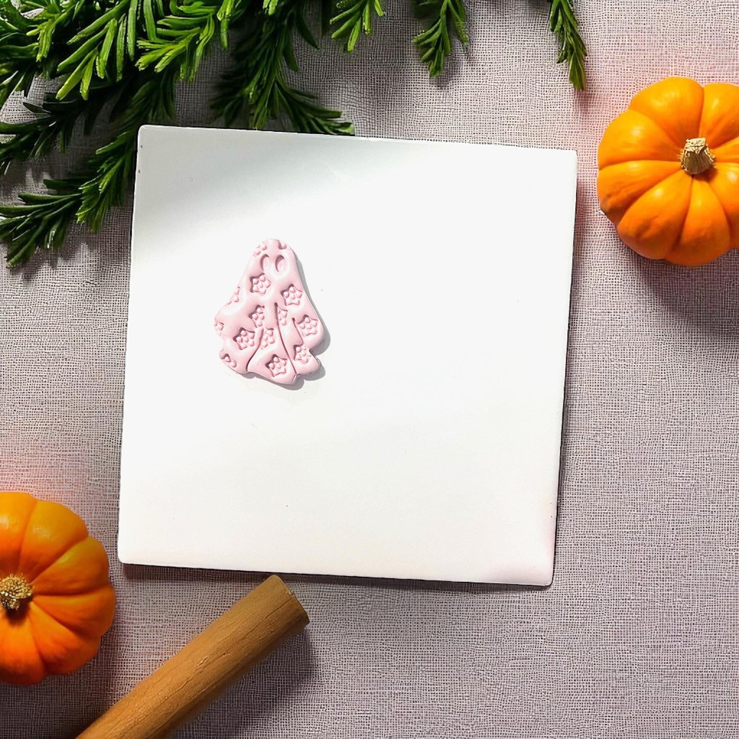 Small pink floral ghost clay piece on white tile with pumpkins