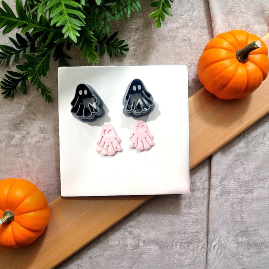 Black ghost cutters with pink clay ghosts beside pumpkins