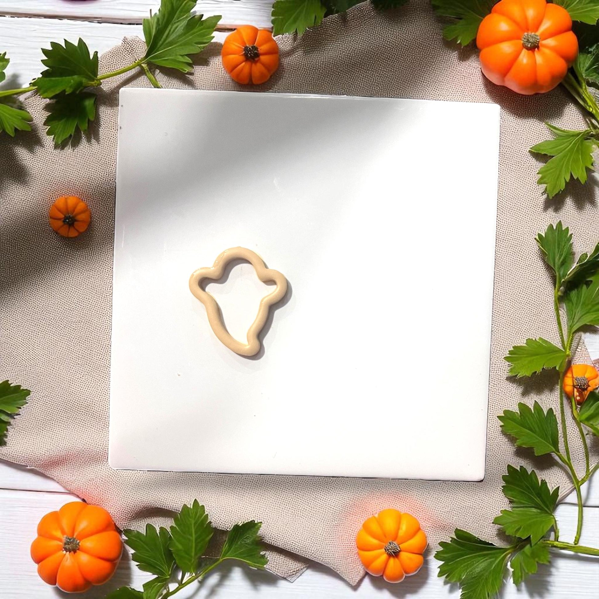 Beige clay thin ghost silhouette surrounded by pumpkins and leaves