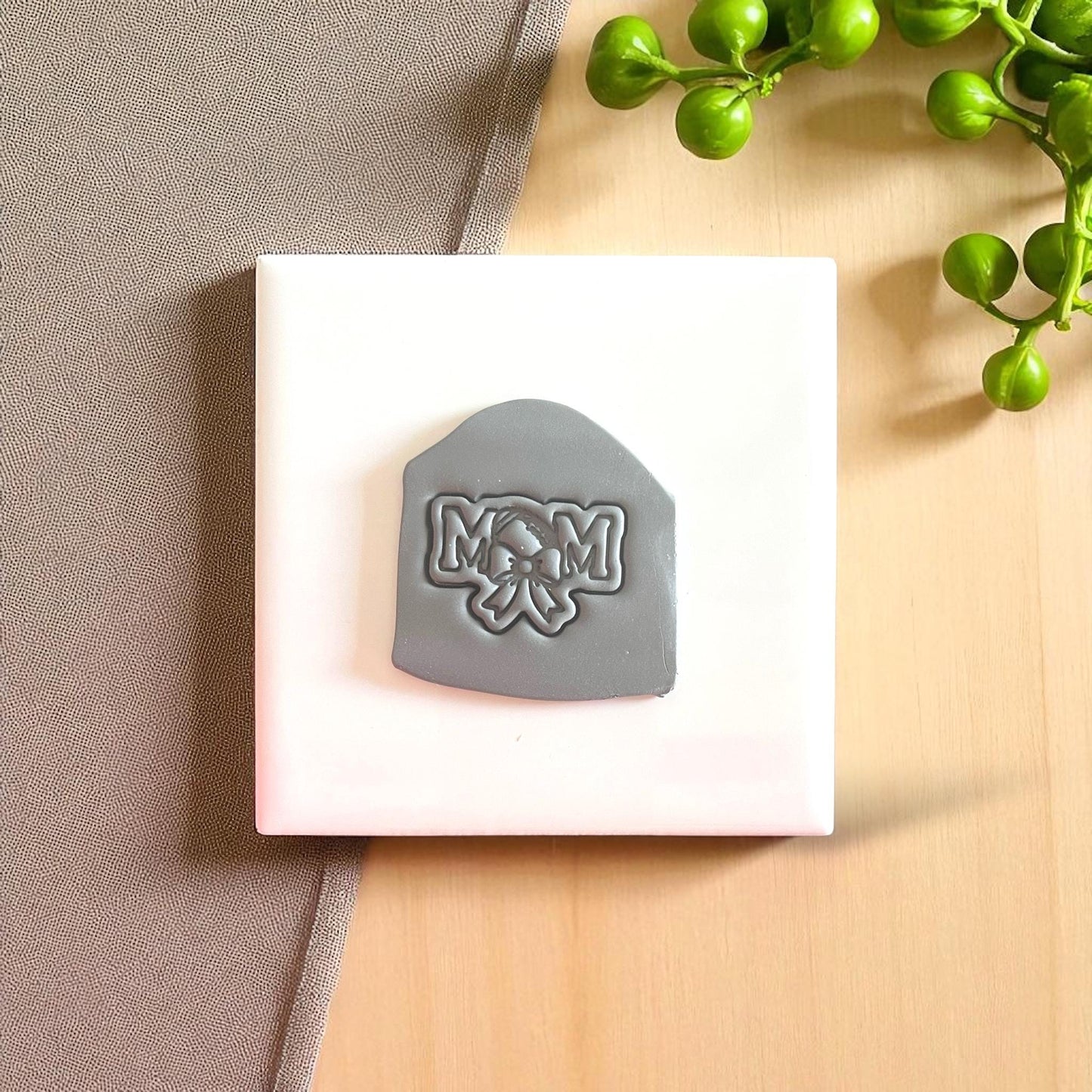 Gray football mom clay imprint with bow design on white tile