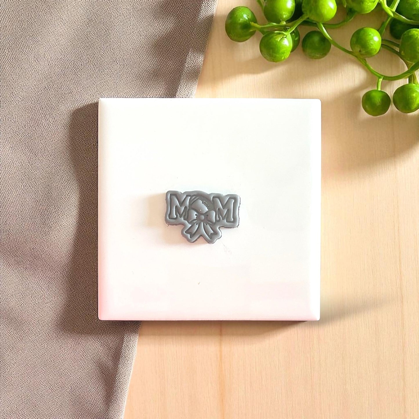 Small gray football mom clay piece with bow on white tile