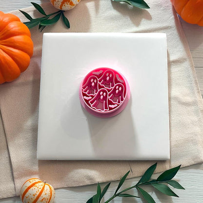 Pink ghost circle clay cutter on white tile surrounded by pumpkins