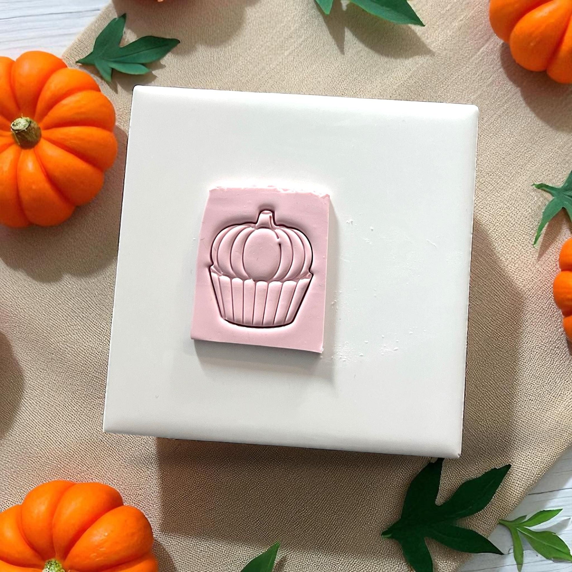 Pumpkin cupcake clay impression and cutter on white tile with pumpkins