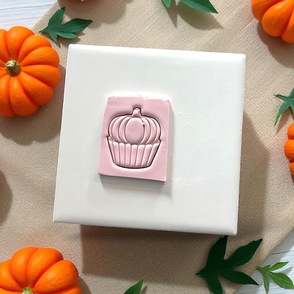 Pumpkin cupcake clay impression and cutter on white tile with pumpkins