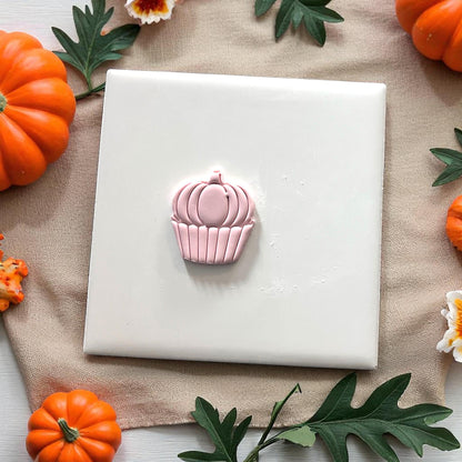 Pink pumpkin cupcake clay design on white tile with pumpkins