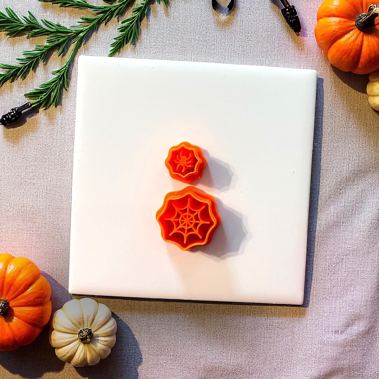Orange spiderweb and spider clay cutters on white tile with pumpkins