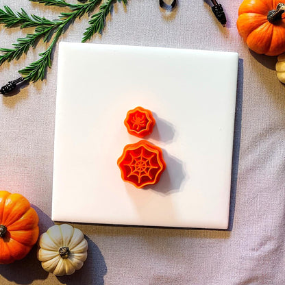 Orange spiderweb and spider clay cutters on white tile with pumpkins