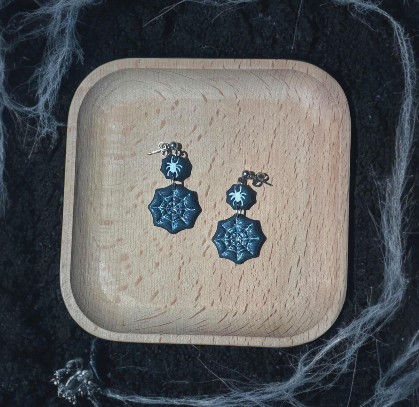 Black spiderweb and spider clay earrings on wooden dish with cobweb background