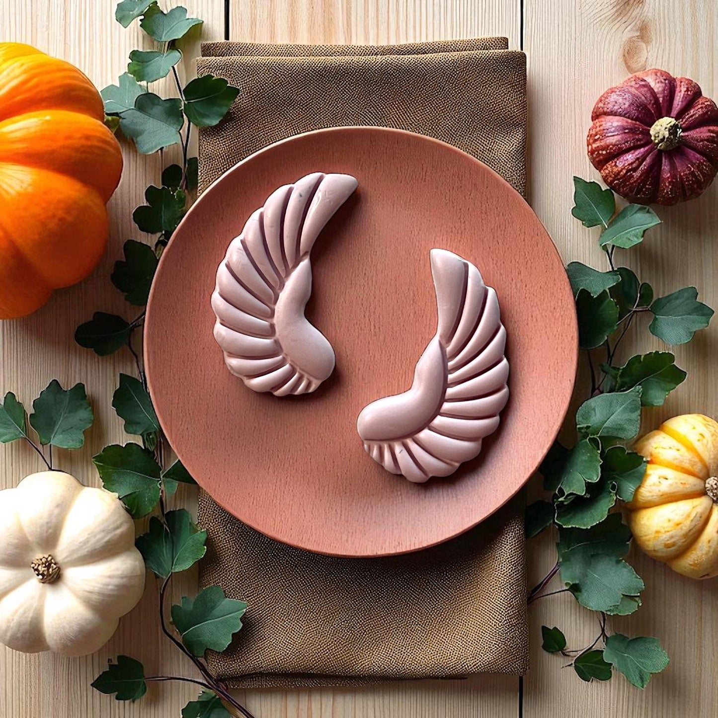 Large pink scarab wing clay pieces on round wooden plate with pumpkins