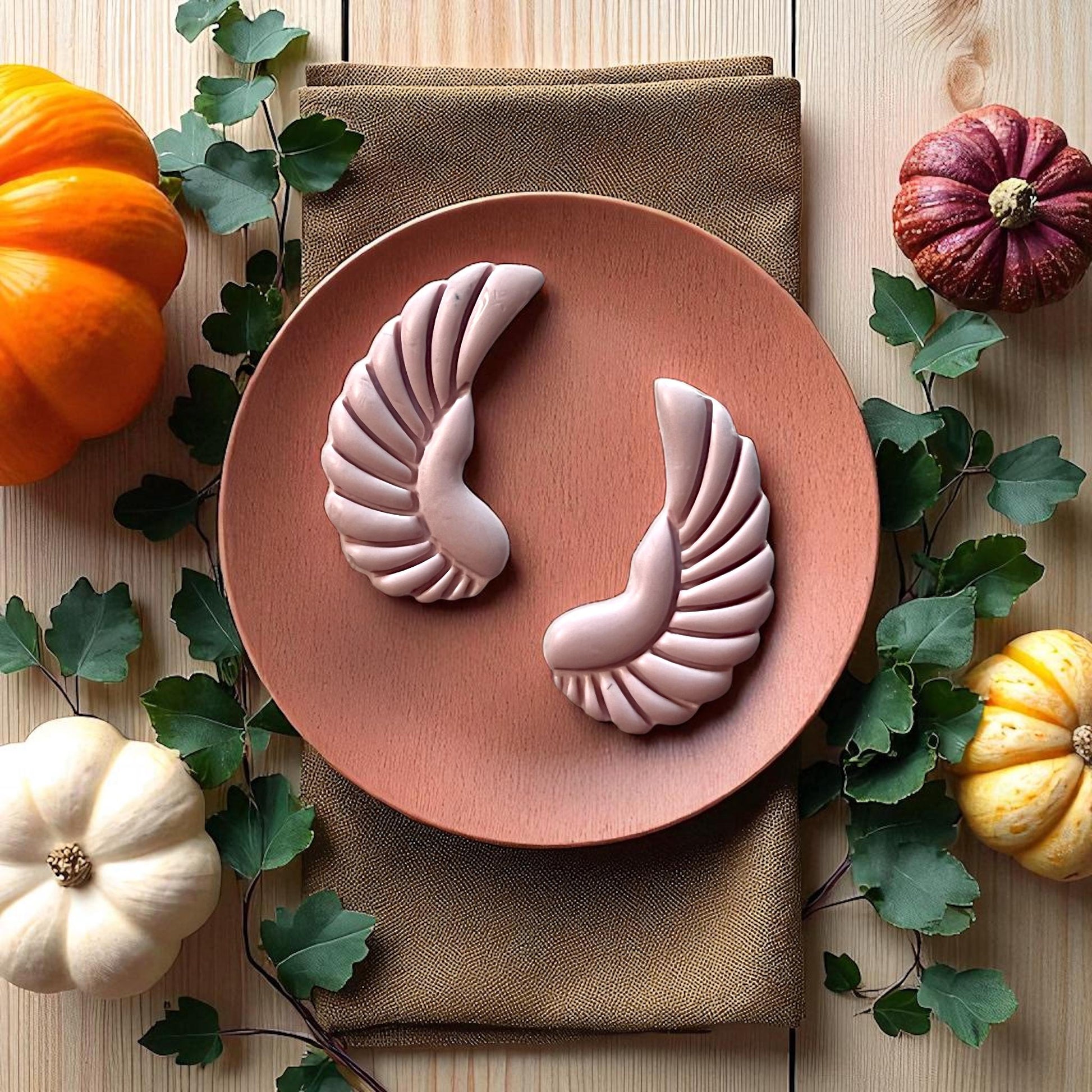 Large pink scarab wing clay pieces on round wooden plate with pumpkins