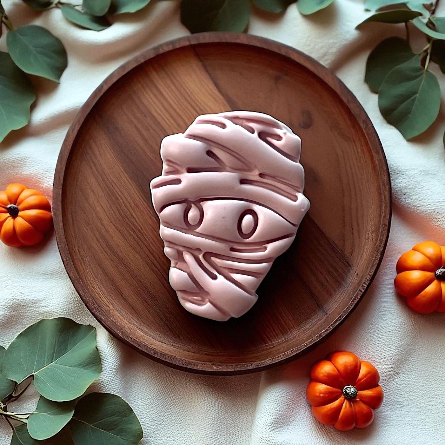 Large pink mummy clay piece on wooden plate with pumpkins and greenery