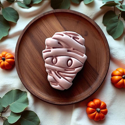 Large pink mummy clay piece on wooden plate with pumpkins and greenery