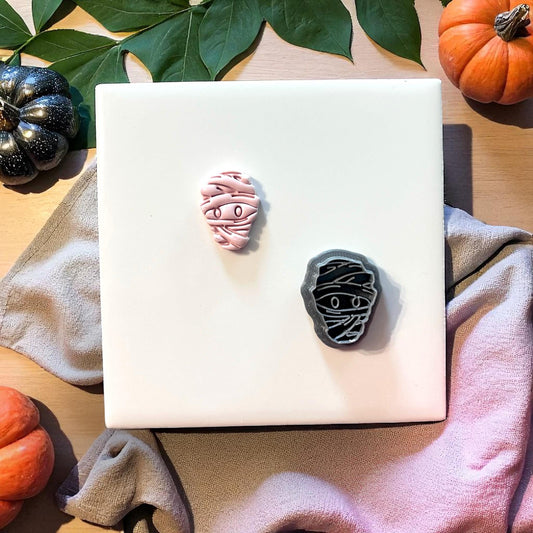 Pink mummy face clay impression with cutter on white tile and pumpkins
