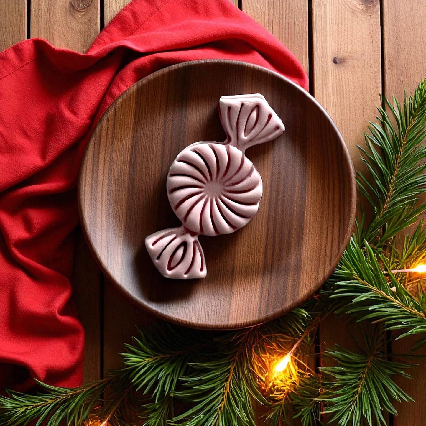 Peppermint candy clay imprint on wooden plate with holiday lights and pine branches
