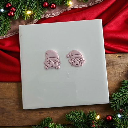 Elf boy and girl clay imprints on white tile with festive greenery and red fabric