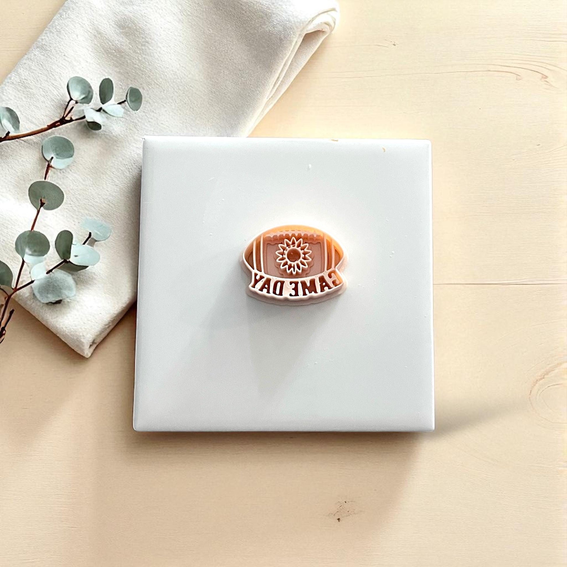 Sunflower football game day clay cutter on white tile with greenery