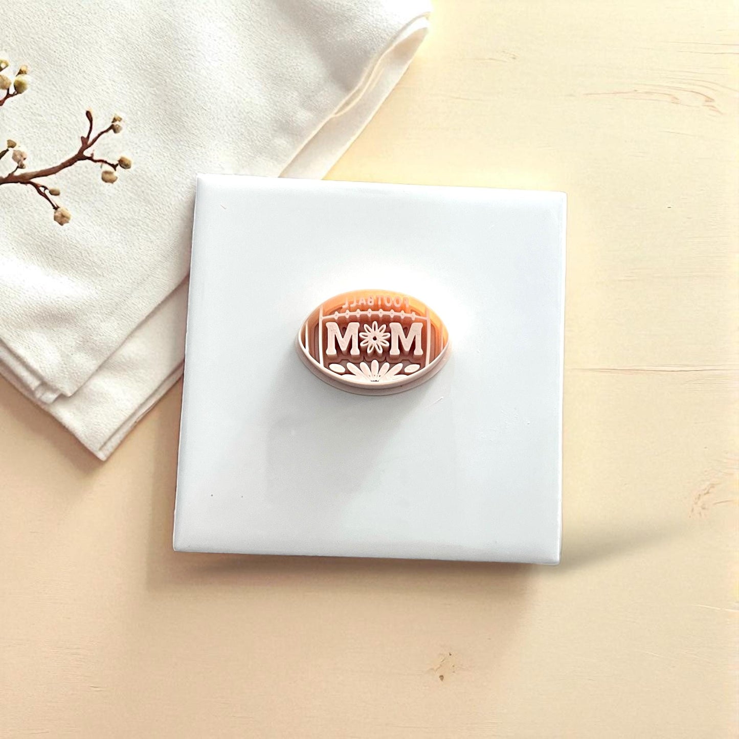 Beige football mom clay cutter with imprint on white tile