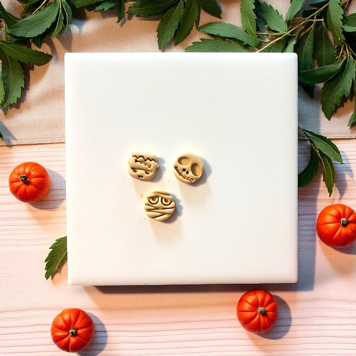 Three clay Halloween character imprints surrounded by pumpkins and greenery