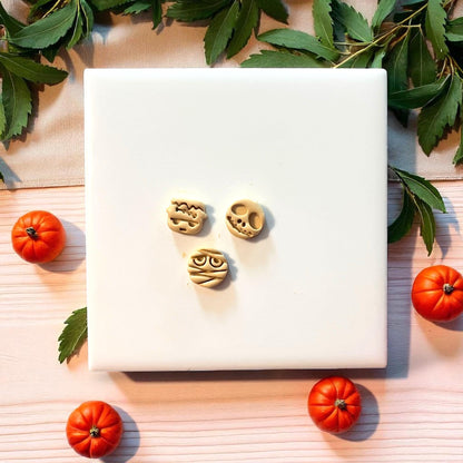 Three clay Halloween character imprints surrounded by pumpkins and greenery